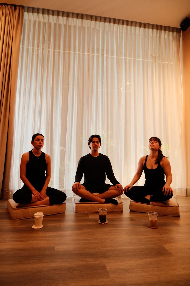 Tres personas meditando frente a una cortina iluminada en MUNA