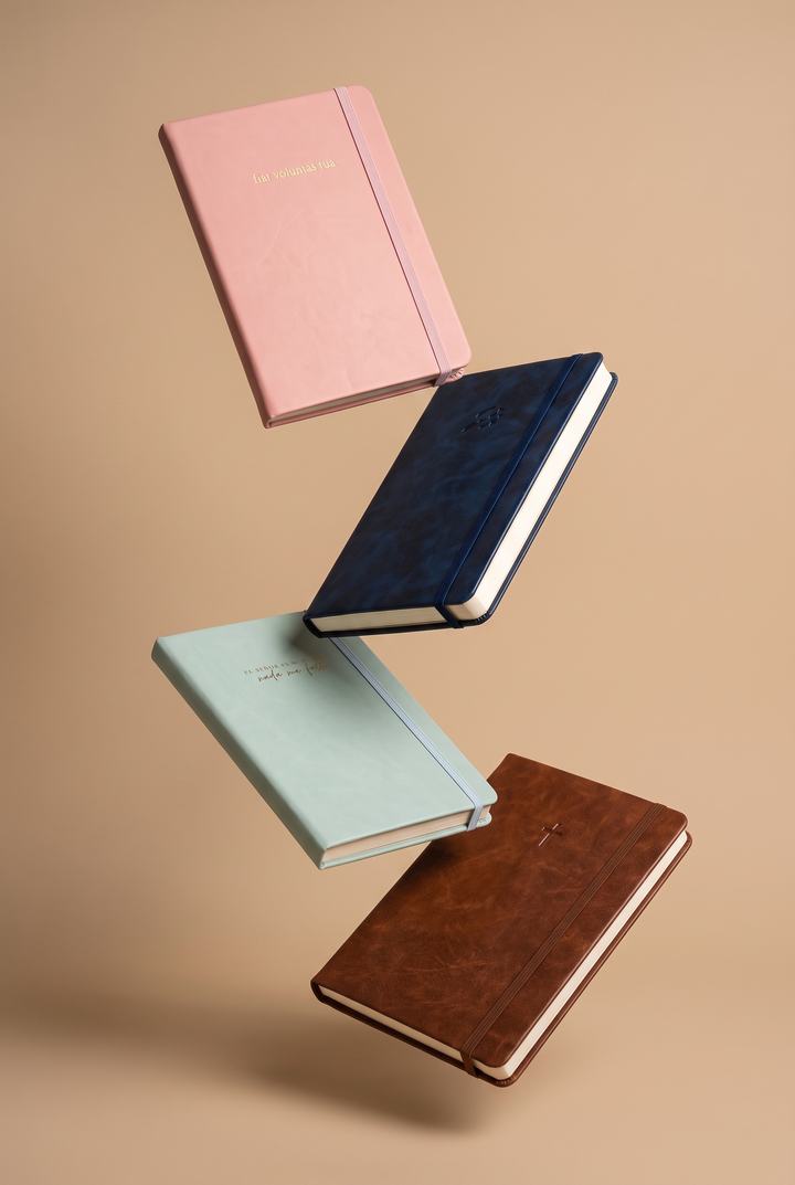 Cuatro cuadernos de colores suspendidos sobre fondo arena